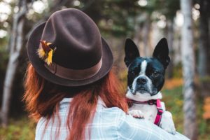the back of a woman carrying a Boston Terrier in the outdoors