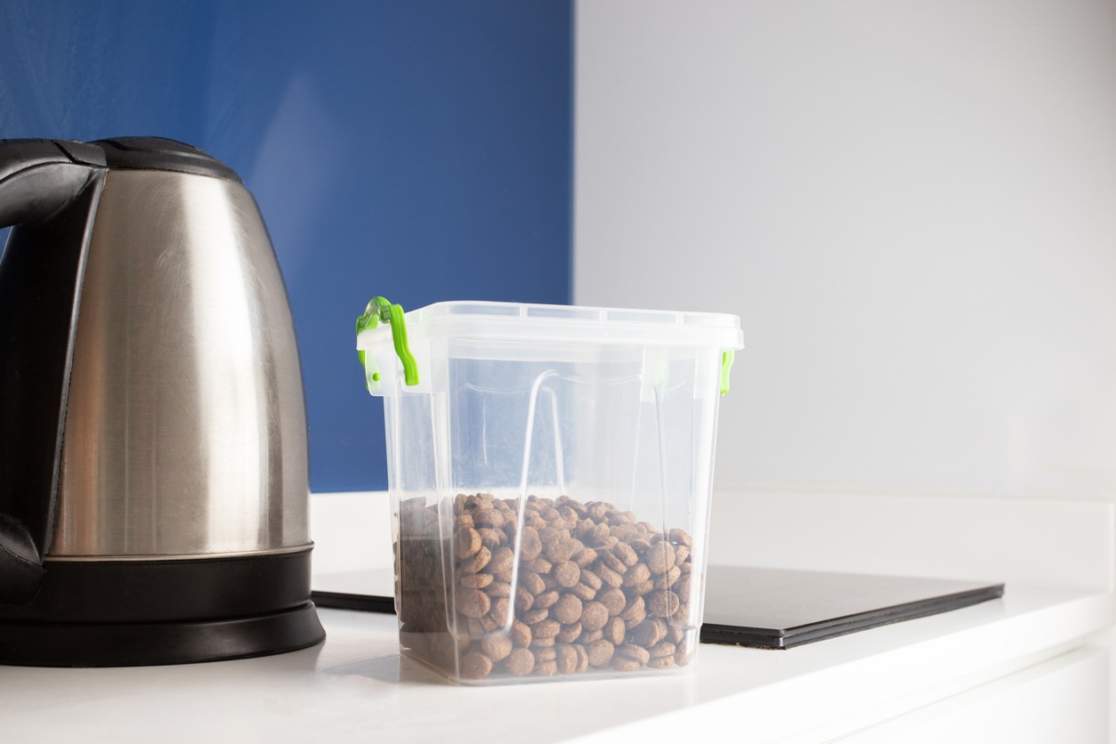 Dog food in a plastic container on a countertop with kettle on the background. 